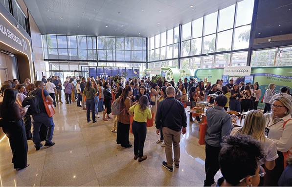 Pessoas em um ambiente interno amplo e iluminado com paredes de vidro participando de um evento ou feira com estandes e intera es diversas.  Description generated by AI