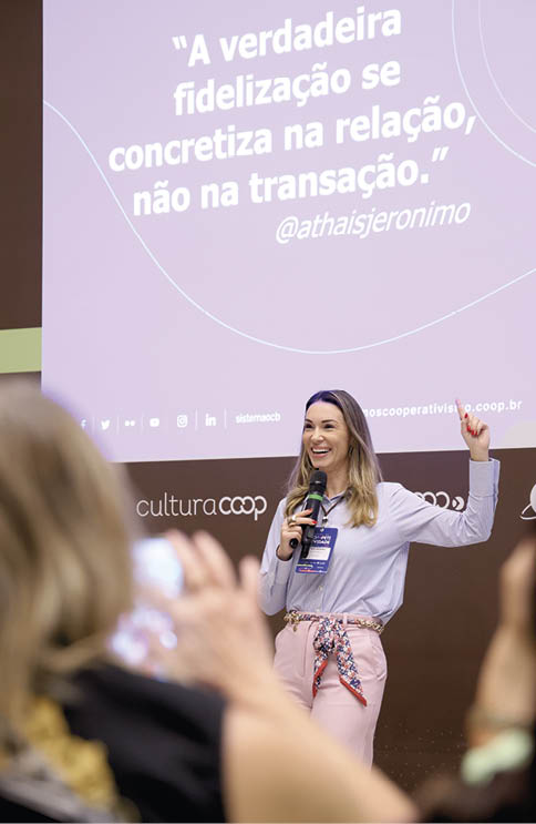 Pessoa sorridente com microfone apresenta palestra em evento com proje o de frase sobre fideliza  o e relacionamento.  Description generated by AI