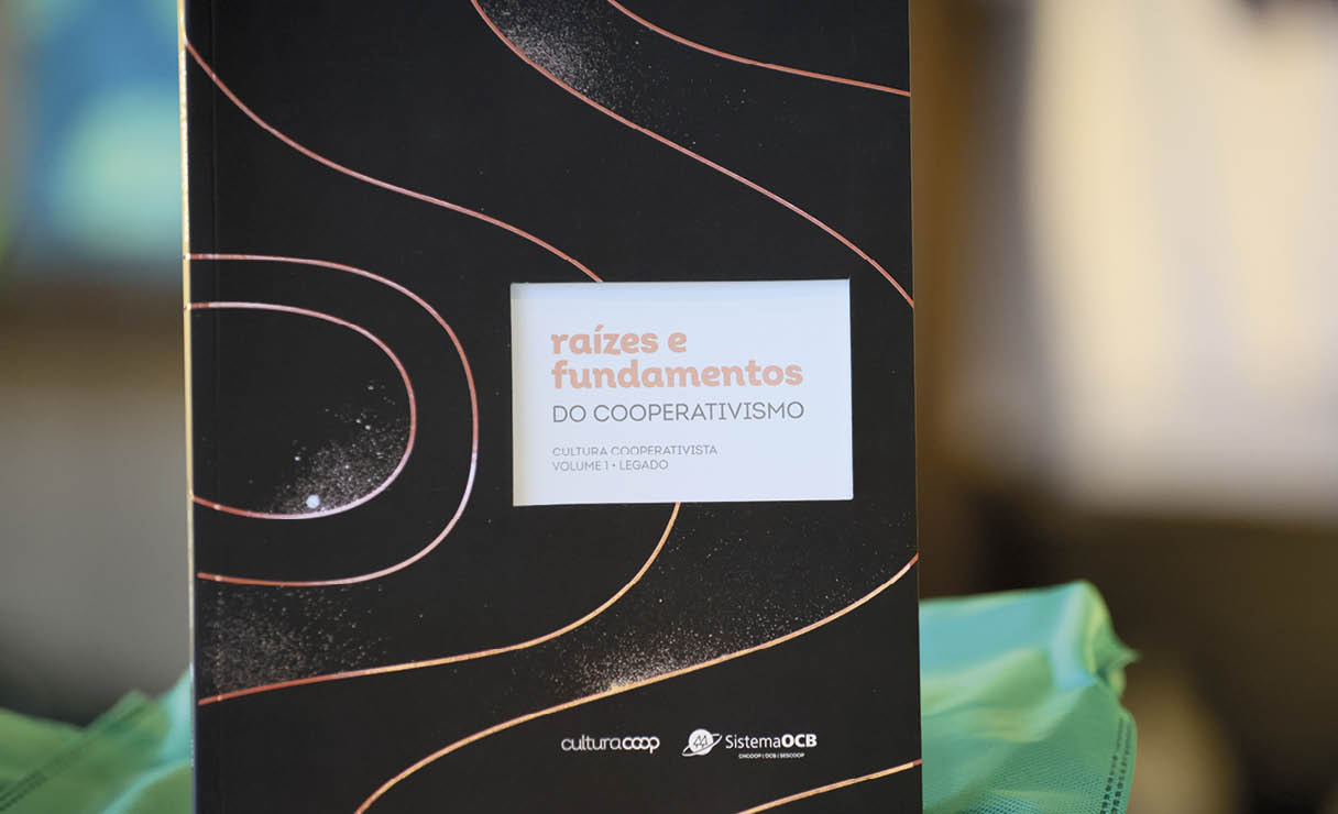 Livro com capa preta e detalhes em linhas curvas laranjas com o t tulo “raizes e fundamentos do cooperativismo" em destaque no centro. Description generated by AI