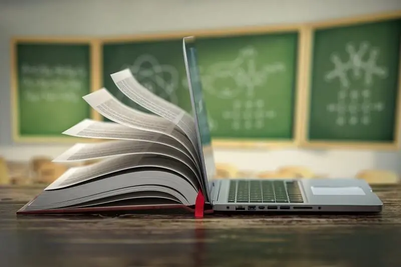 Imagem de um notebook e de um livro aberto para ilustrar a conectividade nas escolas
